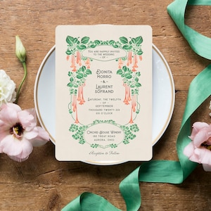 K&ouml;nnte beinhalten: Eine Hochzeitseinladung mit floralem Design, mit den Namen Donita Morro und Laurent Sofrand. Die Einladung ist umgeben von Blumen, einer Ringbox und einem gr&uuml;nen Band auf einer Holzoberfl&auml;che.
