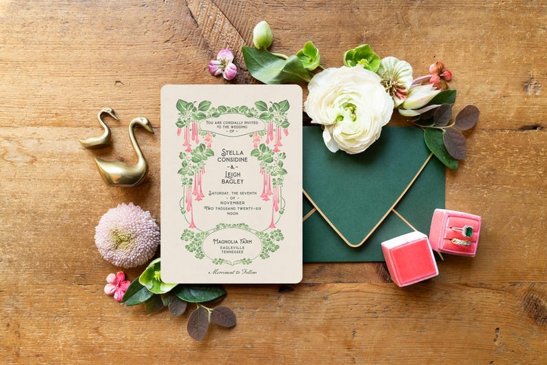 K&ouml;nnte beinhalten: Hochzeitseinladung mit floralem Design, mit den Namen Stella Considine und Leigh Bagley. Enth&auml;lt einen gr&uuml;nen Umschlag, Ringk&auml;stchen, goldene Schwanfiguren und Blumen auf einer Holzoberfl&auml;che.