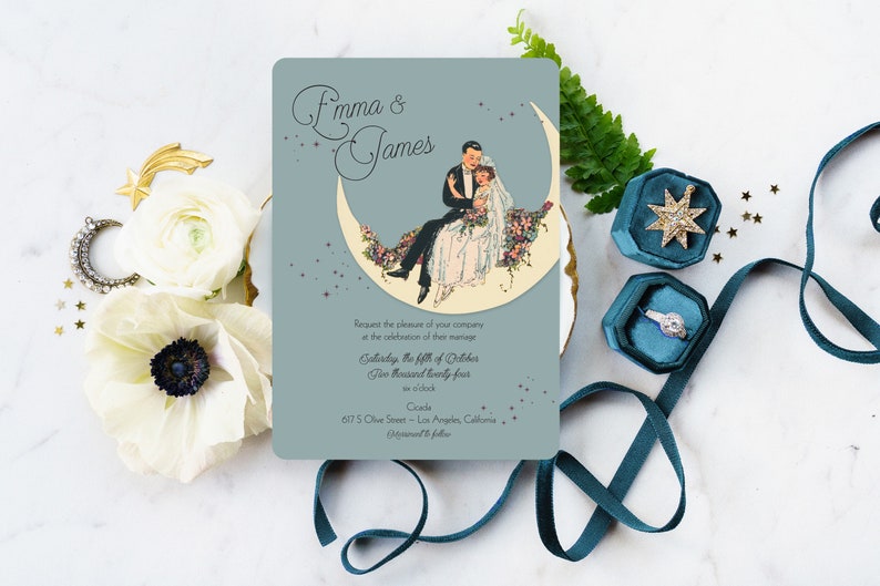 Puede incluir: Una invitaci&oacute;n de boda con un fondo azul y una luna creciente con una pareja sentada en ella. El texto dice "Emma & James" e incluye la fecha y la hora de la boda. La invitaci&oacute;n est&aacute; decorada con estrellas.