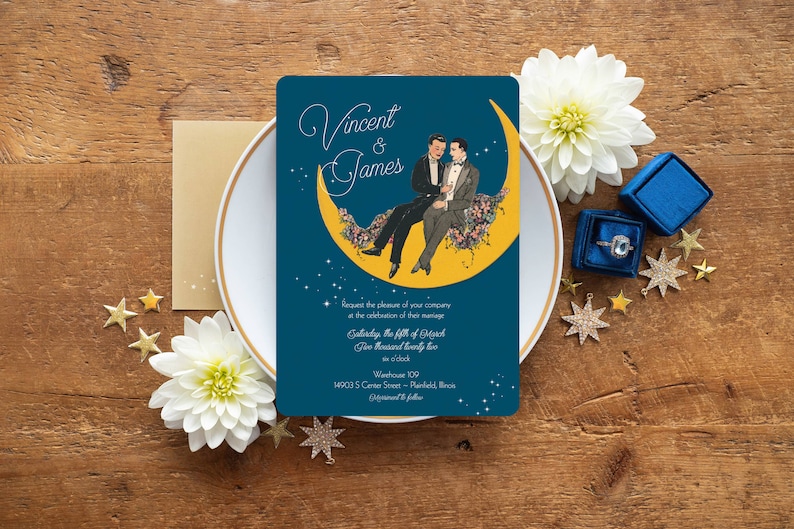 Puede incluir: Una invitaci&oacute;n de boda azul con una luna creciente amarilla y dos hombres con traje sentados en ella. La invitaci&oacute;n dice "Vincent & James" e incluye la fecha, la hora y el lugar de la boda.
