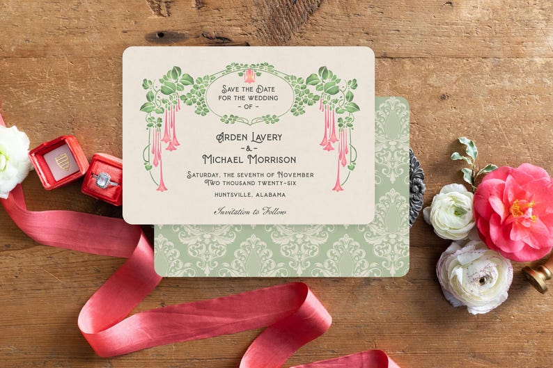 K&ouml;nnte beinhalten: Eine Hochzeitseinladung mit floralem Design, mit den Namen "Arden Lavery" und "Michael Morrison" und dem Datum "Samstag, der siebte November zweitausendsechsundzwanzig." Die Einladung liegt auf einer Holzoberfl&auml;che mit Blumen und einem roten Band.