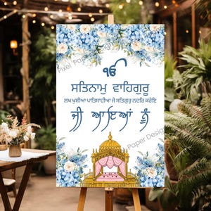 May include: A welcome sign on an easel, featuring floral arrangements and text in a script font. The sign has a white background with blue and white flowers at the top and bottom. The text is in a dark blue color.