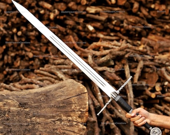 May include: A long, silver sword with a sharp blade and a black handle. The sword has a crossguard and a decorative pommel. The background is a pile of wood. The sword is held by a person.