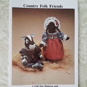 Puede incluir: Un patrón de costura para una muñeca de vaca y una muñeca de oveja de 35,5 cm con ropa. El patrón incluye patrones de tamaño completo e instrucciones fáciles. La imagen muestra una muñeca de vaca en blanco y negro y una muñeca de oveja negra con vestidos de cuadros rojos y azules.