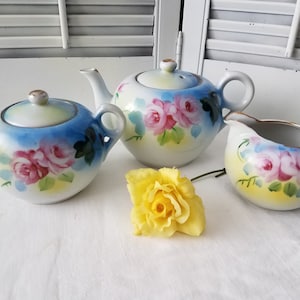 May include: A vintage tea set with a blue and yellow floral design. The set includes a teapot, creamer, and sugar bowl.
