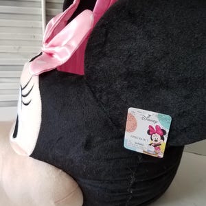 Puede incluir: Una cesta jumbo de Minnie Mouse de peluche en negro, rosa y blanco. La cesta tiene forma de cabeza de Minnie, con grandes orejas negras, un lazo rosa y orejas rosas. Una etiqueta de Disney est&aacute; adjunta.