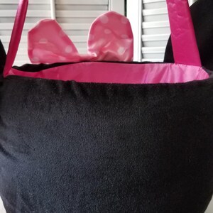 Puede incluir: Bolso tote de felpa negra con forro y asas de sat&eacute;n rosa. El bolso presenta un lazo rosa con lunares blancos. Las asas son de color rosa brillante. El bolso est&aacute; dise&ntilde;ado para parecerse a la cabeza de un personaje.