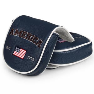 May include: A navy blue leather golf putter headcover with white piping. The front features the embroidered text AMERICA, the letters EST, the number 1776, and a small rectangular patch of the United States flag. The interior is lined with grey fabric.