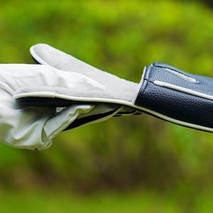 May include: A white golf glove with a black trim at the wrist and a dark blue textured golf club head cover with white piping. The head cover is held horizontally, showing its smooth interior lining and the exterior pebbled leather texture.