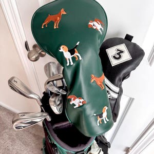 Puede incluir: Una bolsa de palos de golf con una funda verde para la cabeza con dise&ntilde;os de perros bordados. La bolsa incluye varios palos de golf y una funda negra con el n&uacute;mero 3 blanco.