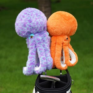 Pode incluir: Duas capas para a cabeça do taco de golfe de polvo de pelúcia. Uma é roxa e azul, a outra laranja. Ambas têm cabeças grandes e redondas, olhos expressivos e múltiplos tentáculos. Elas são projetadas para proteger tacos de golfe.