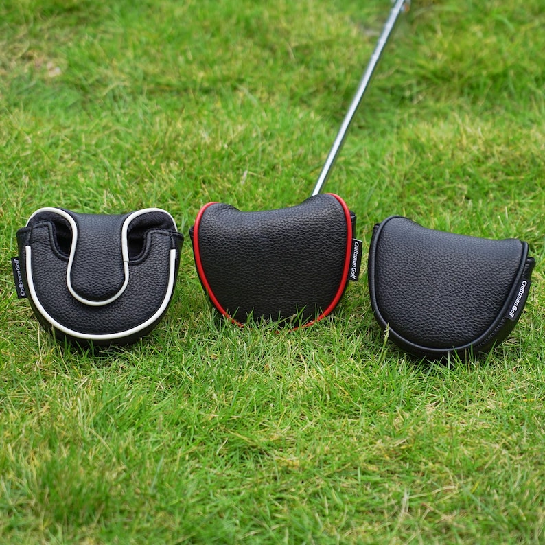 Może przedstawiać: Trzy osłony głowicy puttera golfowego na zielonej trawie. Jedna jest czarna z białym wykończeniem, druga czarna z czerwonym wykończeniem, a trzecia jednolita czarna. Pokrowce mają teksturowany wygląd i widoczna jest nazwa marki "Craftsman Golf".