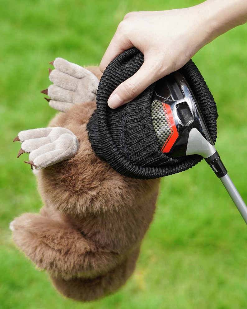 Puede incluir: Una funda para la cabeza del palo de golf de felpa marr&oacute;n con forma de topo, con una parte superior negra de punto tipo gorro. La funda tiene patas de color marr&oacute;n claro con garras. Un palo de golf est&aacute; parcialmente insertado en la funda.