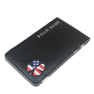 Könnte beinhalten: Schwarzes Portemonnaie mit einem Kleeblatt-Patch mit dem Design der amerikanischen Flagge. Der Text "YOUR NAME" ist in Weiß auf der Oberseite gestickt. Das Portemonnaie hat eine rechteckige Form.