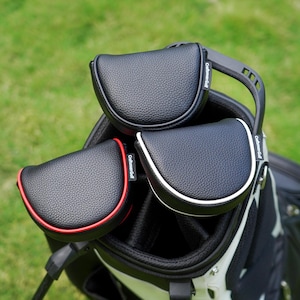 Może przedstawiać: Trzy czarne osłony na gł&oacute;wki kij&oacute;w golfowych o teksturowanych powierzchniach znajdują się w torbie golfowej. Jedna osłona ma czerwone obramowanie, druga białe, a trzecia nie ma obramowania. Torba golfowa jest czarno-biała, z zielonym tłem.