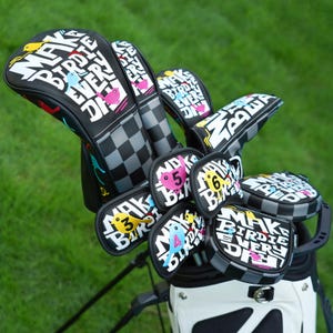 Könnte beinhalten: Ein Set von Golfschlägerhauben und Schlägerprotektoren mit einem schwarz-weißen Schachbrettmuster. Die Bezüge zeigen den Text "MAKE BIRDIE EVERY DAY" und farbenfrohe Vogelillustrationen. Die Golftasche ist weiß.