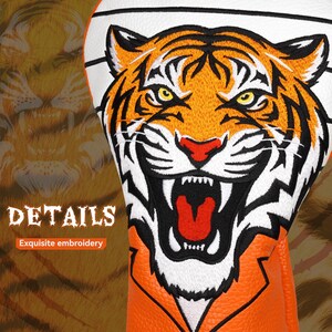 Op de afbeelding: Golfclub hoes met een geborduurd tijgergezicht in oranje, zwart en wit. De hoes heeft een witte bovenkant en een oranje basis. De tekst "DETAILS" en "Exquisite embroidery" zijn zichtbaar.