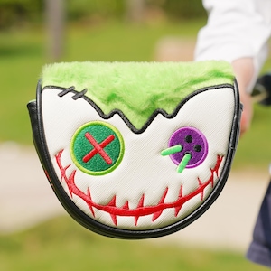 Pode incluir: Uma capa para a cabe&ccedil;a do taco de golfe com um design de rosto de monstro. A capa apresenta um topo verde e difuso, um rosto branco com detalhes costurados e uma borda preta. O rosto tem uma boca costurada vermelha e olhos de bot&atilde;o verdes e roxos.