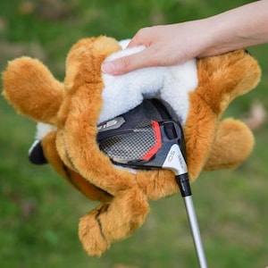 Puede incluir: Una funda para la cabeza del palo de golf con forma de zorro, en tonos marr&oacute;n y blanco, con un palo de golf parcialmente insertado. La funda tiene una textura de felpa y est&aacute; dise&ntilde;ada para proteger la cabeza del palo.