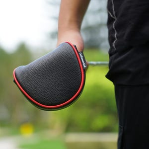 Może przedstawiać: Czarny pokrowiec na gł&oacute;wkę kija golfowego z czerwonym obramowaniem. Pokrowiec ma teksturowaną powierzchnię, widoczny jest napis "Craftsman Golf". Pokrowiec jest trzymany.