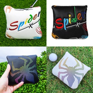 May include: Golf putter head covers in white and black with a spider design. The covers have the word "Spider" embroidered in various colors. One cover is on green grass with a golf ball.
