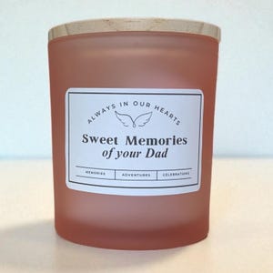 May include: A peach-colored candle with a wooden lid. A white label on the front reads "Always in our hearts Sweet Memories of your Dad." The label also includes the words "Memories," "Adventures," and "Celebrations."