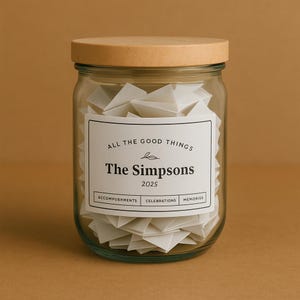 Może przedstawiać: Przezroczysty szklany słoik z drewnianą pokrywką, wypełniony złożonymi białymi karteczkami. Słoik ma białą etykietę z napisem "ALL THE GOOD THINGS", "The Simpsons" i "2025". Etykieta zawiera również słowa "ACCOMPLISHMENTS", "CELEBRATIONS" i "MEMORIES".