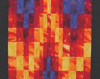 May include: A quilt block with a geometric design in shades of red, orange, yellow, and purple. The design resembles a flame or a stylized W.