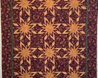 May include: A quilt with a brown background and a pattern of orange stars. The stars are made of fabric with a geometric design. The quilt is surrounded by a green border.