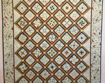 May include: A white quilt with a diamond pattern. The diamonds are outlined in brown, blue, and green. The quilt is made of fabric with a floral pattern.