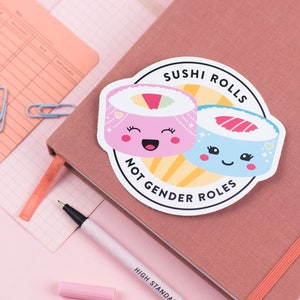 以下が含まれることがあります： 顔が付いた寿司ロール2つの漫画の画像が描かれたピンクとブルーのステッカー。ステッカーには「Sushi Rolls Not Gender Roles」と書かれています。