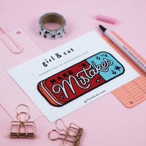 以下が含まれることがあります： 消しゴムの形をした赤いと青いアイロン接着刺繍パッチで、「MAKE Mistakes」という文字が白い筆記体で書かれています。パッチには文字の周りに白い星があり、白いカードに「girl & cat awesome iron-on embroidered patch」と「girlandcat.com」という文字が書かれています。