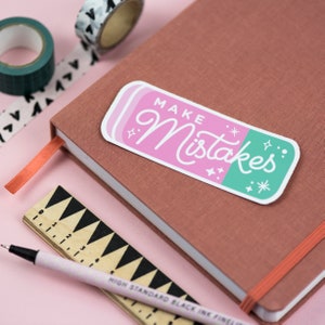 May include: A pink and green eraser sticker with the text "MAKE Mistakes" in white cursive lettering. The sticker has a white border and is decorated with small white stars.