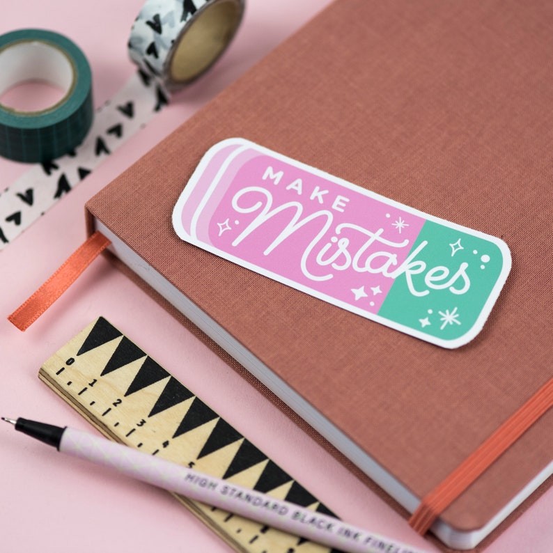 May include: A pink and green eraser sticker with the text "MAKE Mistakes" in white cursive lettering. The sticker has a white border and is decorated with small white stars.