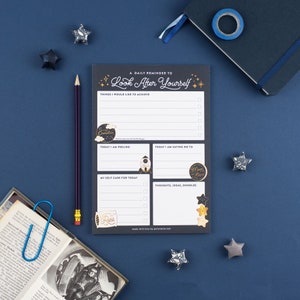 May include: A dark blue notepad with the text "Look After Yourself". It includes sections for daily goals, feelings, and self-care. A pencil, journal, and star decorations are arranged around the notepad.