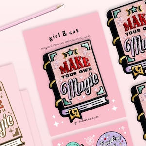 May include: Pink iron-on patch featuring a book design. The book has a pink cover with the text "MAKE YOUR OWN MAGIC" in colourful embroidery. The patch is on a pink background with a white border.