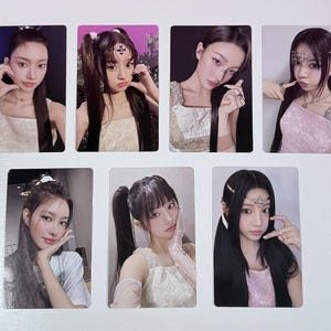 May include: A collection of seven rectangular photo cards featuring young women. Each card showcases a different pose and outfit, with variations in hairstyles and accessories. The cards are arranged on a light-colored surface.