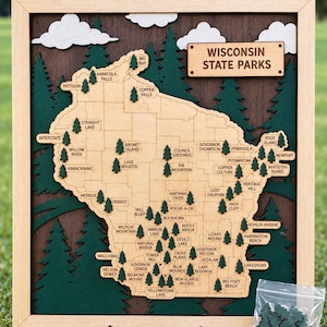 May include: A wooden wall map of Wisconsin State Parks featuring a light-colored map cutout on a dark brown background with green layered pine trees and white clouds. The map includes engraved labels for various parks and a title plaque.