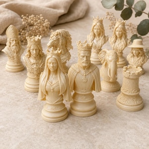 Op de afbeelding: Een verzameling crèmekleurige schaakstukken met gedetailleerde bustes van een koning, koningin, loper, paard en toren. De set bevat figuren met kronen, een olifant en een persoon met een hoed, allemaal vervaardigd met complexe texturen en afwerkingen.