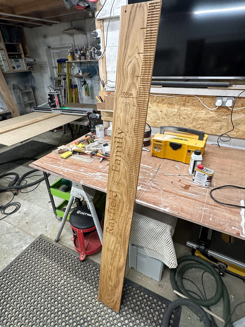Op de afbeelding: Een houten groeimeter met de woorden "Rayfield Family" en metingen in centimeters tot 150 cm.