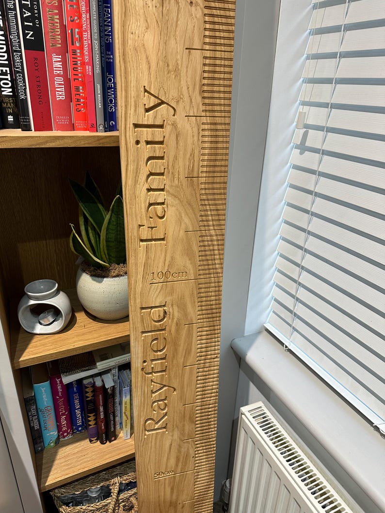 Op de afbeelding: Een houten groeimeter met de tekst "Rayfield Family" en metingen in centimeters. De meter is lichtbruin en heeft een natuurlijke houtnerf.