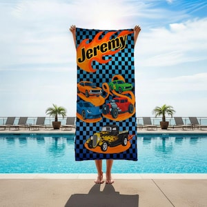 May include: A personalised beach towel with the name "Jeremy" in yellow script and an orange flame design. The towel has a blue and black chequered background and illustrations of five colourful cars.