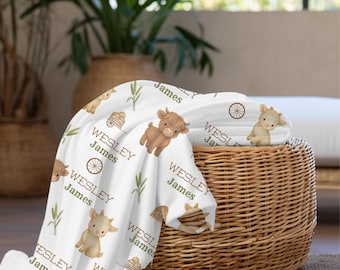 May include: A white baby blanket with a repeating pattern of cartoon farm animals, wheat, and wagon wheels. The blanket has the name "Wesley James" printed on it in a green font. The blanket is draped over a wicker basket.