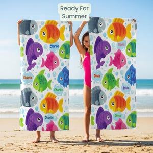 Peut inclure: Serviette de plage avec un motif de poissons colorés dans les tons orange, violet, rose, vert et bleu. Le texte "Ready For Summer" est en haut. Les noms "Charlie" et "Olivia" sont également sur la serviette.