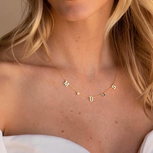 Può includere: Una delicata collana d'oro con le lettere M, B e S. La collana ha piccole pietre preziose tra le lettere. La collana è indossata intorno al collo.