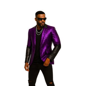 May include: A purple sequin blazer with black leather sleeves. The blazer is paired with a black shirt, black pants, and sunglasses. A silver chain necklace adds a touch of elegance to the outfit.