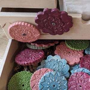 Könnte beinhalten: Eine Schublade gefüllt mit bunten Keramik-Schubladengriffen mit filigranen Mandala-Mustern. Die Griffe sind in den Farben Rosa, Grün, Blau und Lila.