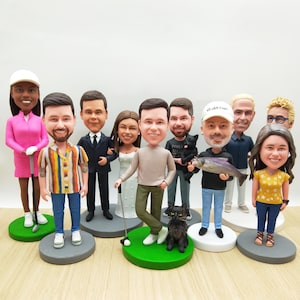 May include: A collection of custom bobblehead figurines, each depicting a person with unique features and attire. The figurines stand on individual bases, some with green turf, and include accessories like a golf club and a black cat.