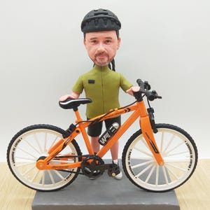Peut inclure: Figurine d'une personne en chemise verte et short noir, portant un casque noir, debout derrière un vélo orange. Le vélo a des roues blanches et le texte "EXTREME FREEDOM" sur le cadre.