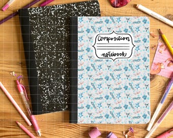May include: Composition notebook with a light blue cover featuring a pattern of stars, feathers, and bows. A black and white composition notebook is next to it. Pencils and pens in pink, purple, and yellow are scattered around the notebooks on a wooden surface.